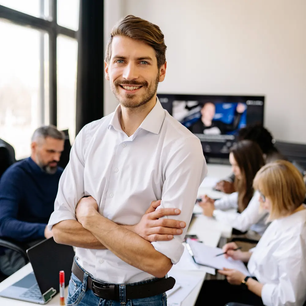 A team leader smiling in front of his colleagues working hard.