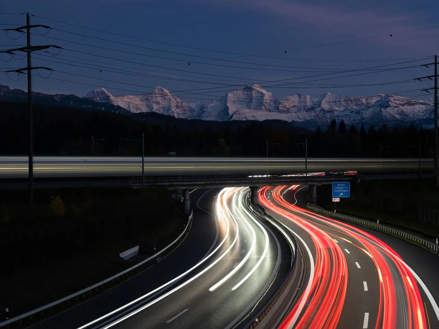 Light trails at night showing fast cars on a highway in front of scenic mountains